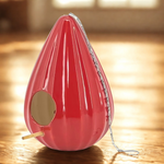 Red birdhouse with a wooden perch on a wooden floor