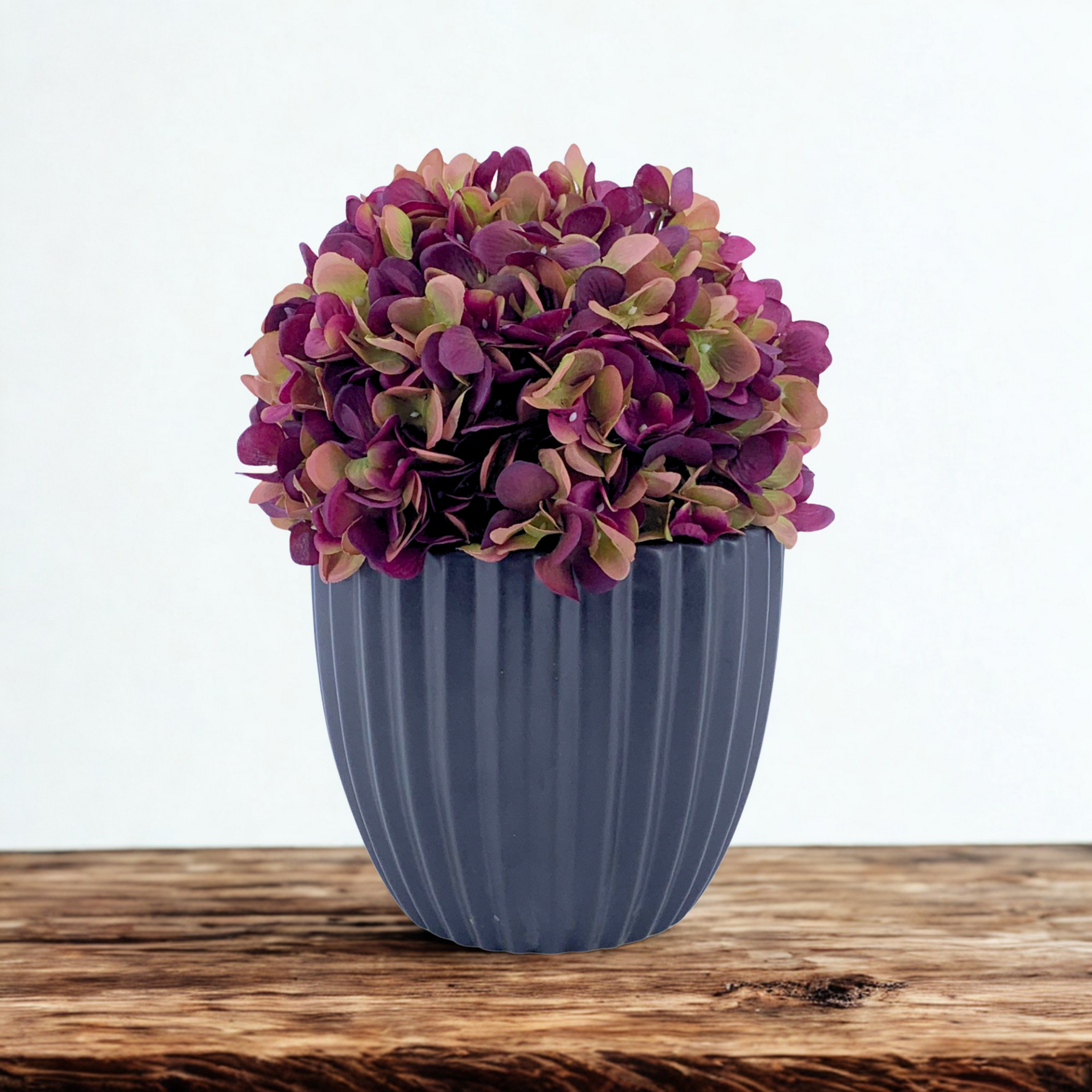 Artificial hydrangea with varying purple colors in a Matte Black Ribbed Ceramic, on a wooden countertop with a white background, by House of Silk Flowers